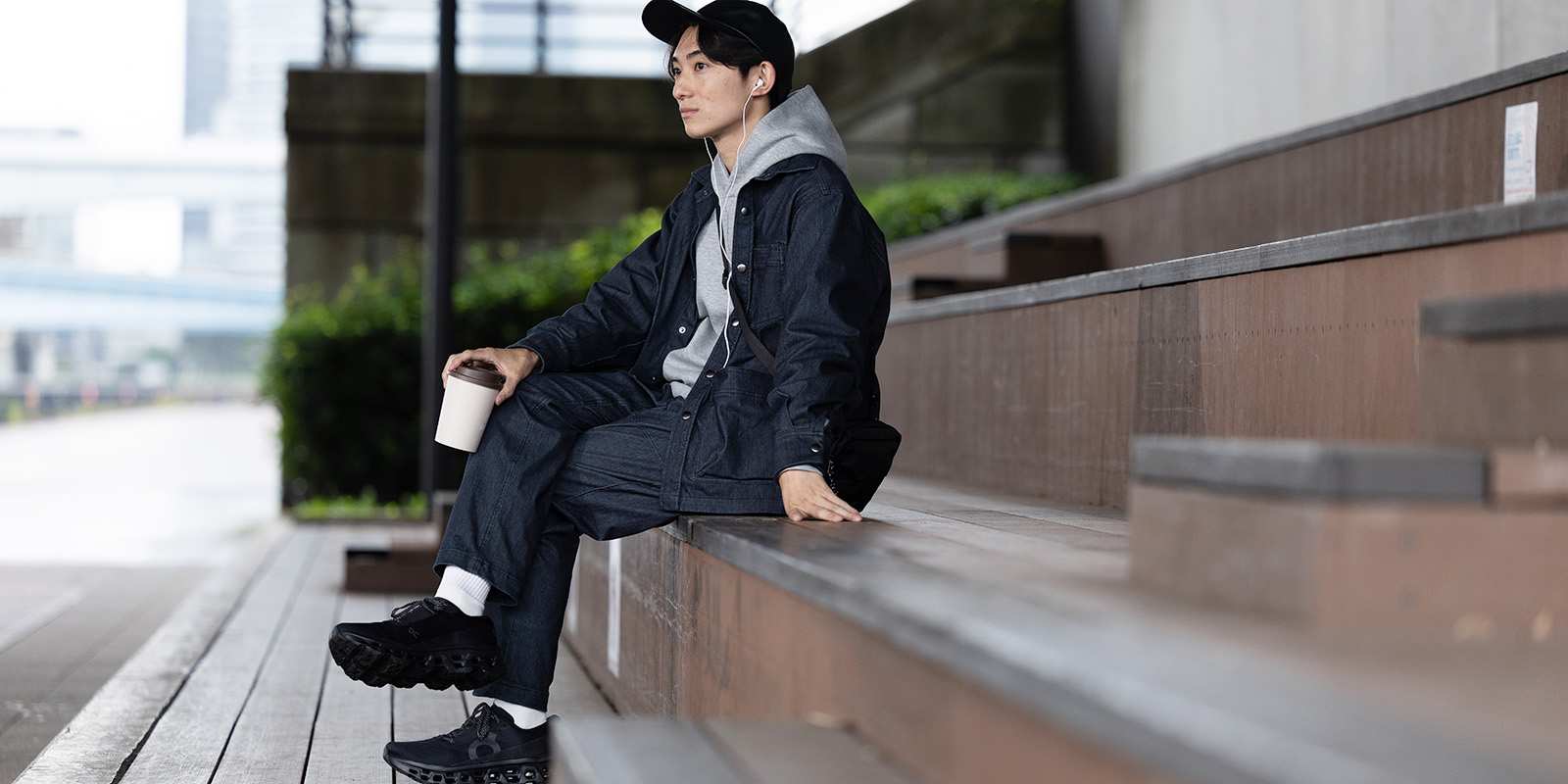 ストレッチデニムのジャケットとパンツで、段差に脚を組んで座る男性